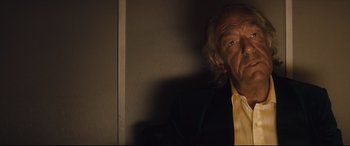 Movie still from “Layer Cake” (2004), directed by Matthew Vaughn – An older man in a yellow shirt and a yellow tie; Close Up shot, Low angle
