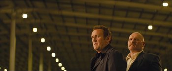 Movie still from “Layer Cake” (2004), directed by Matthew Vaughn – A man in a black shirt and black jacket looking to his left; Medium shot, Low angle