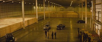 Movie still from “Layer Cake” (2004), directed by Matthew Vaughn – A group of people standing in a large warehouse; Extreme Wide shot, High angle