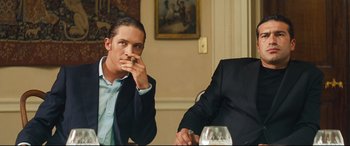 Movie still from “Layer Cake” (2004), directed by Matthew Vaughn – A man sitting at a table with a glass of wine in front of him; Medium shot, Low angle