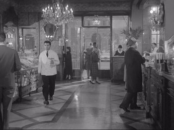 Movie still from “The Girlfriends” (1955), directed by Michelangelo Antonioni – A black - and - white photo of people walking in a store; Wide shot, High angle