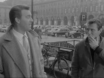 Movie still from “The Girlfriends” (1955), directed by Michelangelo Antonioni – Two men are standing on the sidewalk in front of parked cars; Medium shot, Over the shoulder angle