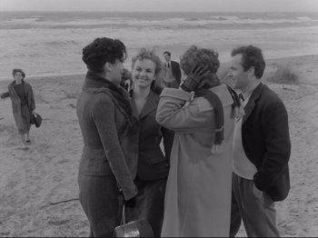 Movie still from “The Girlfriends” (1955), directed by Michelangelo Antonioni – A group of people standing on top of a sandy beach; Medium shot, Over the shoulder angle