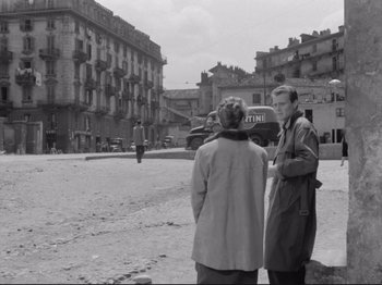 Movie still from “The Girlfriends” (1955), directed by Michelangelo Antonioni – Two people standing on a beach in front of some buildings; Wide shot, Over the shoulder angle