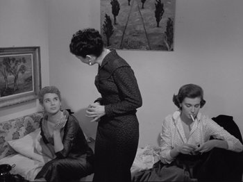 Movie still from “The Girlfriends” (1955), directed by Michelangelo Antonioni – A woman standing next to two other women in a room; Medium shot, High angle