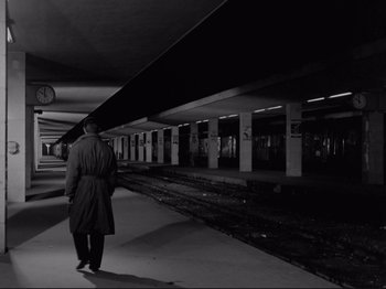 Movie still from “The Girlfriends” (1955), directed by Michelangelo Antonioni – A man in a trench coat walking on a train platform; Wide shot, Low angle