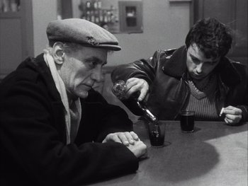 Movie still from “Le Beau Serge” (1958), directed by Claude Chabrol – Two men sitting at a table with a bottle of wine; Medium shot, High angle