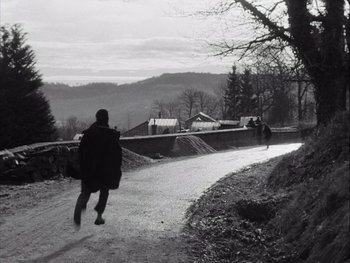 Movie still from “Le Beau Serge” (1958), directed by Claude Chabrol – A man walking down a road with a backpack; Extreme Wide shot, High angle