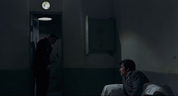 Movie still from “The Red Circle” (1970), directed by Jean-Pierre Melville – A man sitting on a chair next to a person in a room; Wide shot, High angle