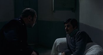 Movie still from “The Red Circle” (1970), directed by Jean-Pierre Melville – Two men sitting on a couch in a dark room; Medium shot, High angle