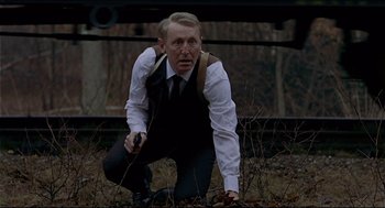 Movie still from “The Red Circle” (1970), directed by Jean-Pierre Melville – A man crouching on the ground holding a cell phone; Medium shot, Over the shoulder angle