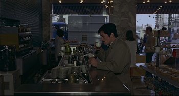Movie still from “The Red Circle” (1970), directed by Jean-Pierre Melville – A man is drinking a cup of coffee at a bar; Medium shot, High angle