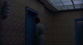 Movie still from “The Red Circle” (1970), directed by Jean-Pierre Melville – A man standing in front of an open door in a dark room; Wide shot, High angle