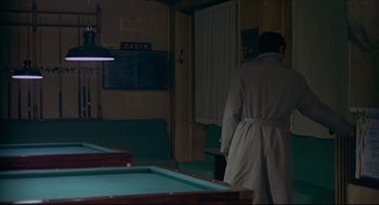 Movie still from “The Red Circle” (1970), directed by Jean-Pierre Melville – A man standing in a room next to a pool table; Wide shot, Over the shoulder angle