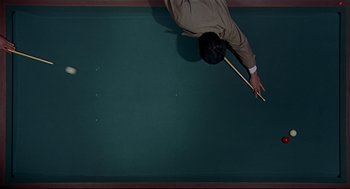 Movie still from “The Red Circle” (1970), directed by Jean-Pierre Melville – A man in a tan suit is playing pool on a pool table; Extreme Close Up shot, Overhead angle