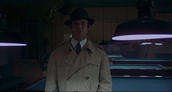 Movie still from “The Red Circle” (1970), directed by Jean-Pierre Melville – A man wearing a trench coat and a hat standing in front of a pool table; Medium shot, Low angle