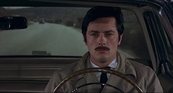 Movie still from “The Red Circle” (1970), directed by Jean-Pierre Melville – A man with a mustache sitting in the drivers seat of a car; Close Up shot, High angle