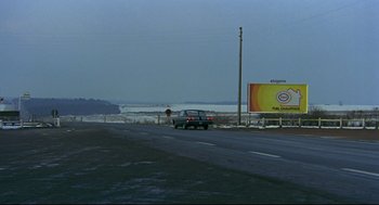 Movie still from “The Red Circle” (1970), directed by Jean-Pierre Melville – A car driving down a road next to a sign; Extreme Wide shot, High angle
