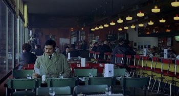 Movie still from “The Red Circle” (1970), directed by Jean-Pierre Melville – A man sitting at a table in front of a group of people; Wide shot, High angle