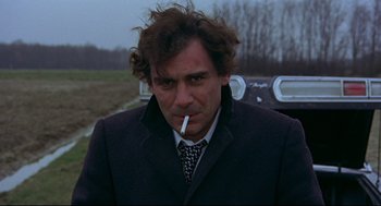 Movie still from “The Red Circle” (1970), directed by Jean-Pierre Melville – A man in a suit and tie smoking a cigarette; Close Up shot, Low angle