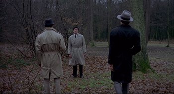 Movie still from “The Red Circle” (1970), directed by Jean-Pierre Melville – A group of men standing in the woods wearing trench coats and fedora hats; Wide shot, High angle