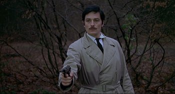 Movie still from “The Red Circle” (1970), directed by Jean-Pierre Melville – A man in a trench coat and tie holding a gun; Medium shot, Low angle