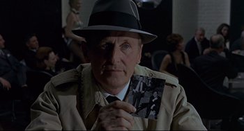 Movie still from “The Red Circle” (1970), directed by Jean-Pierre Melville – A man in a fedora holding an old photo; Close Up shot, Over the shoulder angle