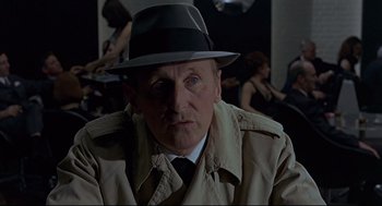 Movie still from “The Red Circle” (1970), directed by Jean-Pierre Melville – A person wearing a hat and a trench coat; Close Up shot, Over the shoulder angle