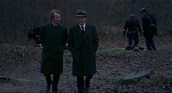 Movie still from “The Red Circle” (1970), directed by Jean-Pierre Melville – Two men in coats and a hat standing in the woods; Medium shot, Over the shoulder angle