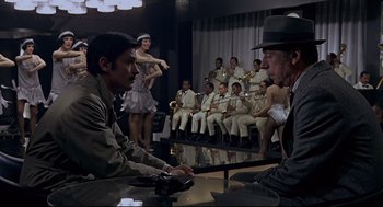 Movie still from “The Red Circle” (1970), directed by Jean-Pierre Melville – A group of men sitting in front of each other in a room; Wide shot, Over the shoulder angle