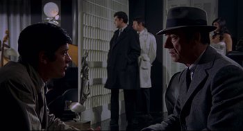 Movie still from “The Red Circle” (1970), directed by Jean-Pierre Melville – A group of men standing next to each other in a room; Medium shot, Over the shoulder angle