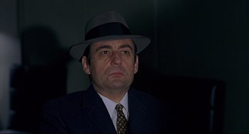 Movie still from “The Red Circle” (1970), directed by Jean-Pierre Melville – A man wearing a suit and a hat; Close Up shot, Low angle