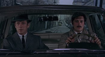 Movie still from “The Red Circle” (1970), directed by Jean-Pierre Melville – Two men sitting in the back seat of a car; Medium shot, High angle