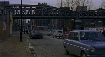 Movie still from “The Red Circle” (1970), directed by Jean-Pierre Melville – Cars are driving down a street under a bridge; Extreme Wide shot, High angle