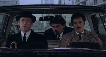 Movie still from “The Red Circle” (1970), directed by Jean-Pierre Melville – A group of men sitting in the back seat of a car; Medium shot, High angle