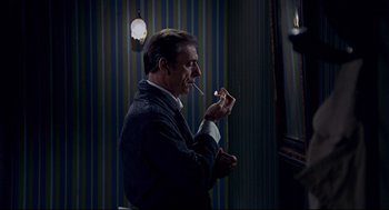 Movie still from “The Red Circle” (1970), directed by Jean-Pierre Melville – A man is smoking a cigarette in a room; Medium shot, Over the shoulder angle