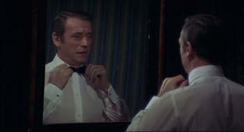 Movie still from “The Red Circle” (1970), directed by Jean-Pierre Melville – A man in a white shirt is fixing his bow tie in front of a mirror; Close Up shot, Over the shoulder angle