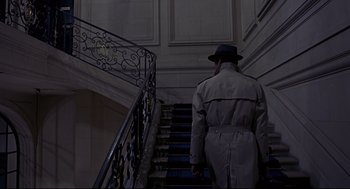 Movie still from “The Red Circle” (1970), directed by Jean-Pierre Melville – A man in a trench coat and hat walking down a flight of stairs; Wide shot, High angle