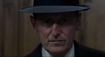 Movie still from “The Red Circle” (1970), directed by Jean-Pierre Melville – A person wearing a suit and a hat; Close Up shot, Low angle