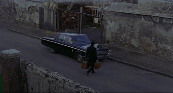 Movie still from “The Red Circle” (1970), directed by Jean-Pierre Melville – A man walking down the street with two suitcases; Extreme Wide shot, High angle