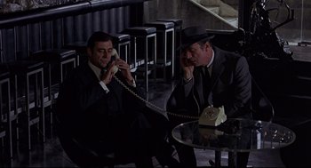 Movie still from “The Red Circle” (1970), directed by Jean-Pierre Melville – Two men sitting at a table talking on the phone; Wide shot, High angle