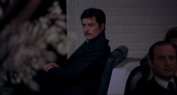 Movie still from “The Red Circle” (1970), directed by Jean-Pierre Melville – A man sitting in a chair wearing a black suit; Medium shot, High angle