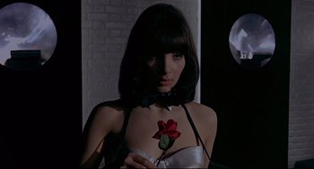 Movie still from “The Red Circle” (1970), directed by Jean-Pierre Melville – A woman with a rose on her chest in front of a brick wall; Close Up shot, High angle