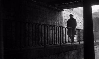 Movie still from “Le Doulos” (1962), directed by Jean-Pierre Melville – A man walking down the side of a bridge; Wide shot, Low angle