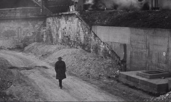 Movie still from “Le Doulos” (1962), directed by Jean-Pierre Melville – A man walking down a dirt road near a building; Wide shot, High angle