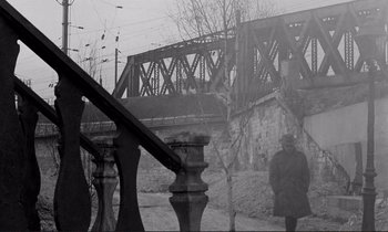 Movie still from “Le Doulos” (1962), directed by Jean-Pierre Melville – A man standing next to a bridge on a foggy day; Wide shot, Low angle