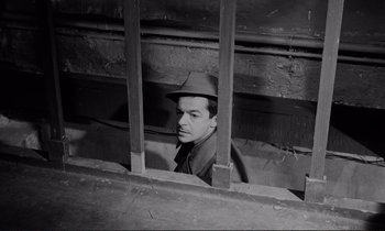 Movie still from “Le Doulos” (1962), directed by Jean-Pierre Melville – A black and white photo of a man wearing a hat; Medium shot, High angle