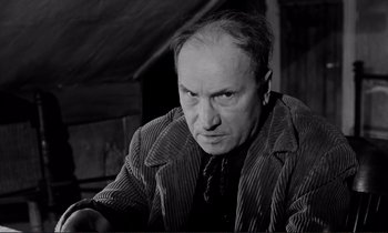 Movie still from “Le Doulos” (1962), directed by Jean-Pierre Melville – An older man in a striped jacket looking at the camera; Close Up shot, Low angle