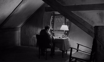 Movie still from “Le Doulos” (1962), directed by Jean-Pierre Melville – A person sitting at a table in a room with a lamp; Wide shot, High angle