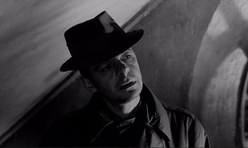 Movie still from “Le Doulos” (1962), directed by Jean-Pierre Melville – A man wearing a hat and a black jacket; Close Up shot, Low angle